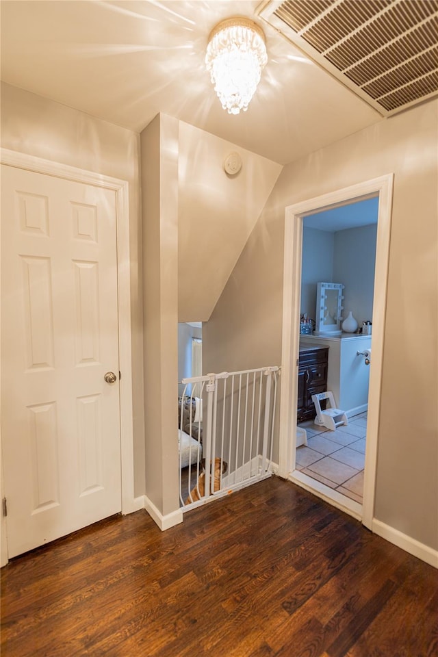 corridor with dark wood-type flooring and an inviting chandelier