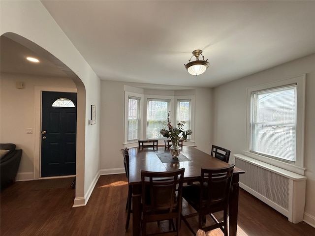 dining room with dark wood-style floors, arched walkways, radiator, and baseboards