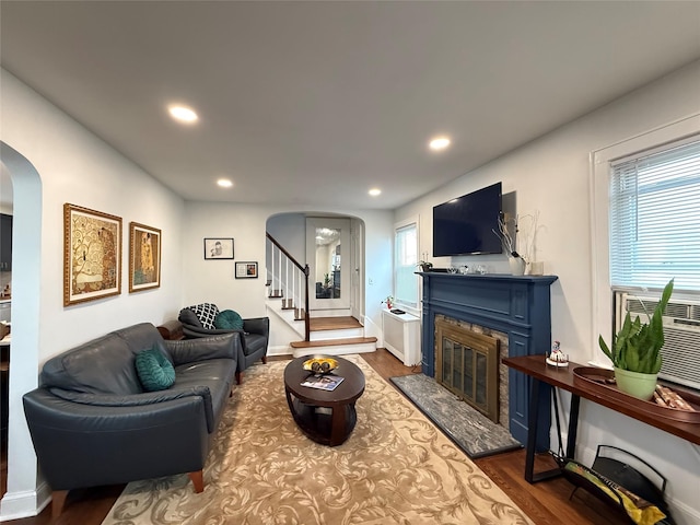 living room featuring dark wood-style floors, arched walkways, recessed lighting, stairway, and a glass covered fireplace