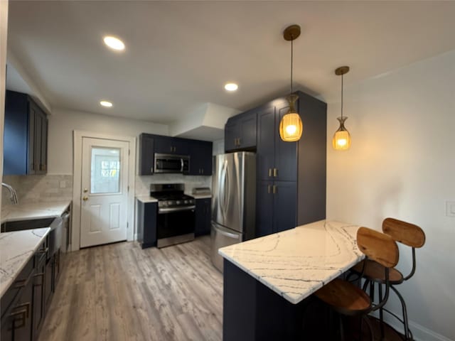 kitchen featuring a peninsula, appliances with stainless steel finishes, a kitchen bar, and light stone counters