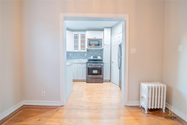 kitchen featuring decorative backsplash, radiator heating unit, light hardwood / wood-style floors, and appliances with stainless steel finishes