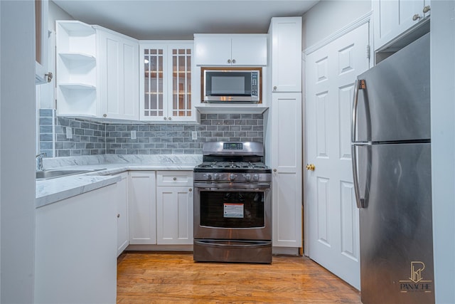 kitchen featuring appliances with stainless steel finishes, white cabinetry, decorative backsplash, light stone counters, and light hardwood / wood-style floors