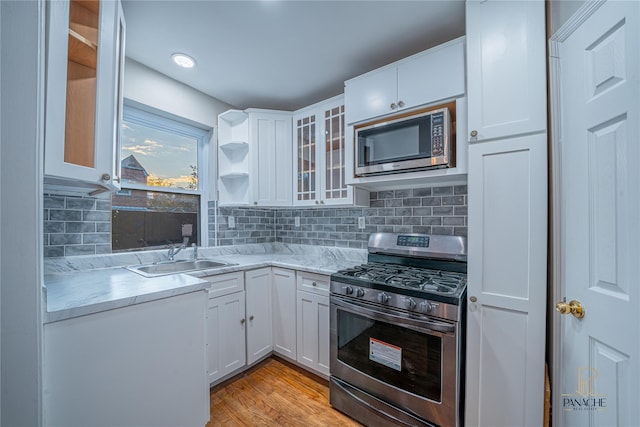 kitchen with tasteful backsplash, white cabinetry, sink, stainless steel appliances, and light wood-type flooring