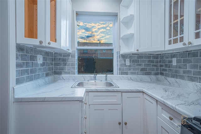 kitchen with white cabinetry, sink, backsplash, and light stone counters