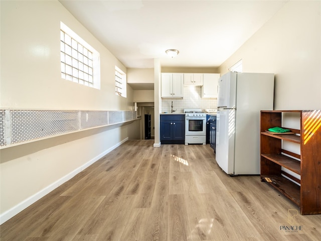 kitchen with gas stove, white cabinetry, light wood-type flooring, white fridge, and backsplash