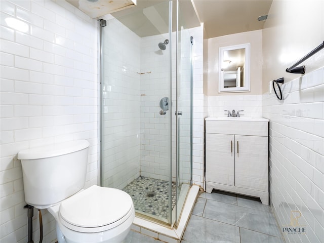 bathroom with tile walls, vanity, walk in shower, toilet, and tile patterned floors