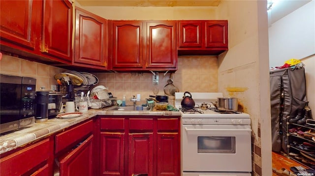 kitchen featuring sink, tile counters, decorative backsplash, and white gas range oven