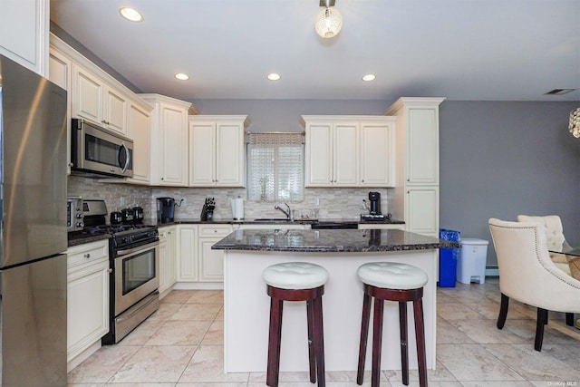 kitchen with sink, decorative backsplash, dark stone counters, a center island, and stainless steel appliances