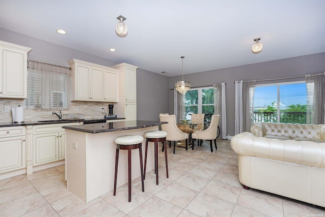 kitchen with sink, tasteful backsplash, decorative light fixtures, a center island, and dark stone counters