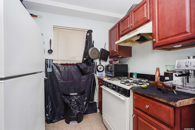 kitchen featuring dark stone countertops, light tile patterned floors, and white appliances