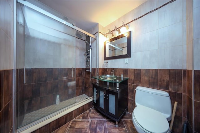 bathroom with a shower with door, vanity, tile walls, and toilet