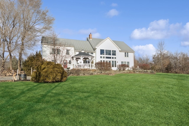 rear view of house with metal roof, a gazebo, a lawn, and a chimney