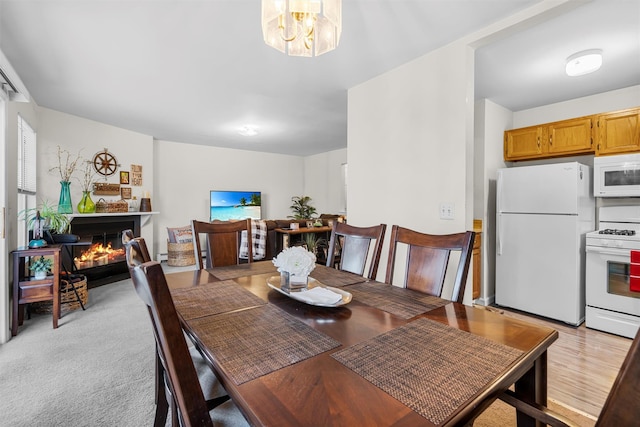 dining space with a warm lit fireplace, light colored carpet, and an inviting chandelier