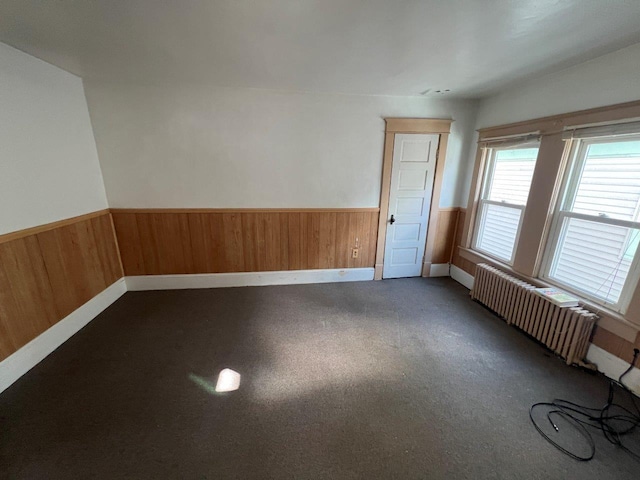 carpeted spare room featuring radiator heating unit and wooden walls