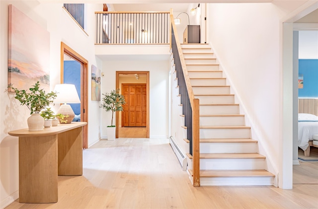 entryway with light hardwood / wood-style floors, a baseboard heating unit, and a high ceiling