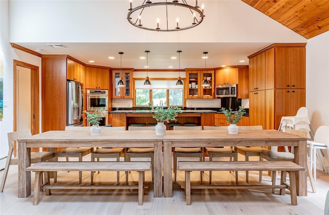 kitchen with light wood-type flooring, stainless steel appliances, hanging light fixtures, an inviting chandelier, and vaulted ceiling