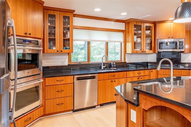 kitchen featuring dark stone countertops, sink, decorative light fixtures, light hardwood / wood-style floors, and stainless steel appliances