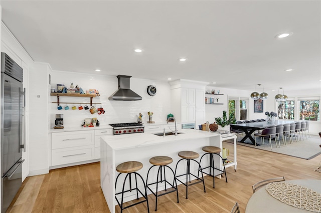 kitchen featuring an island with sink, white cabinetry, stainless steel appliances, and wall chimney exhaust hood