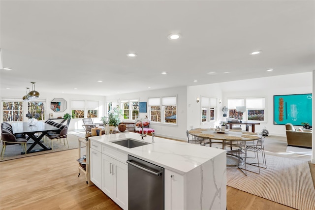 kitchen featuring an island with sink, sink, stainless steel dishwasher, light stone counters, and white cabinets