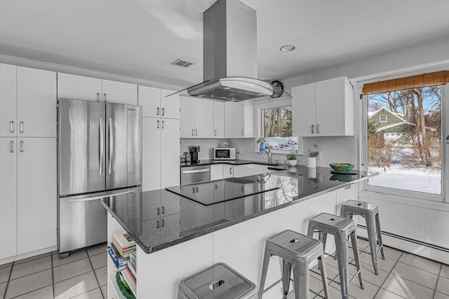 kitchen featuring light tile patterned flooring, a breakfast bar area, island range hood, appliances with stainless steel finishes, and white cabinets