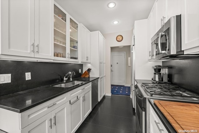 kitchen featuring sink, dark tile patterned floors, appliances with stainless steel finishes, white cabinetry, and tasteful backsplash