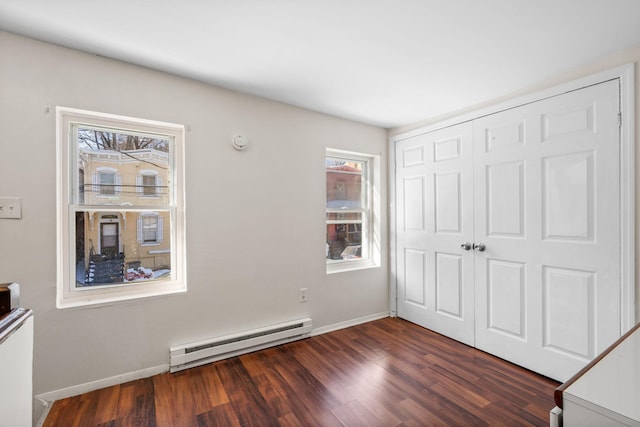 unfurnished bedroom featuring a baseboard heating unit, dark hardwood / wood-style flooring, and a closet