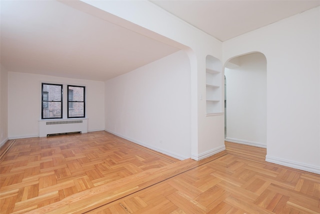 unfurnished room with baseboards, built in shelves, arched walkways, and radiator