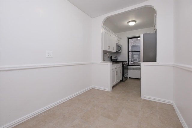 kitchen featuring arched walkways, stainless steel appliances, baseboards, and white cabinets