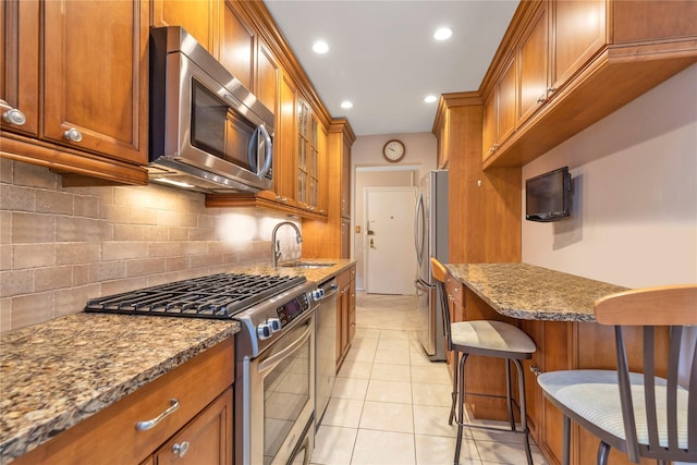 kitchen with appliances with stainless steel finishes, a breakfast bar area, stone counters, light tile patterned flooring, and backsplash