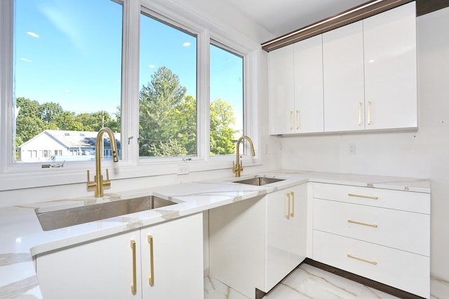 kitchen featuring light stone counters, sink, and white cabinets