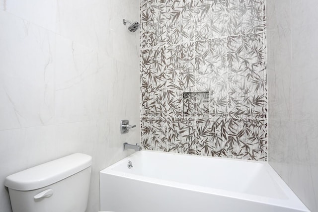 bathroom featuring tiled shower / bath, toilet, and tile walls