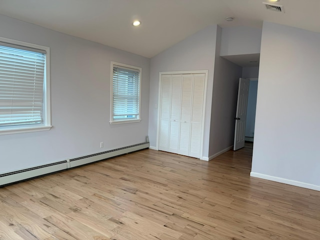 unfurnished bedroom featuring light wood-type flooring, a closet, vaulted ceiling, and baseboard heating