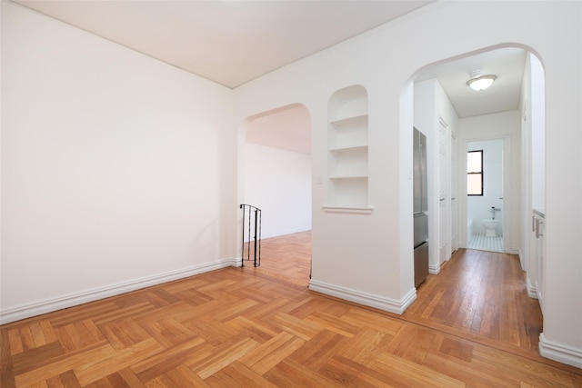 corridor featuring arched walkways, baseboards, and built in features