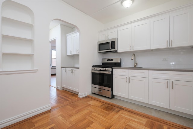 kitchen with white cabinets, decorative backsplash, stainless steel appliances, open shelves, and a sink