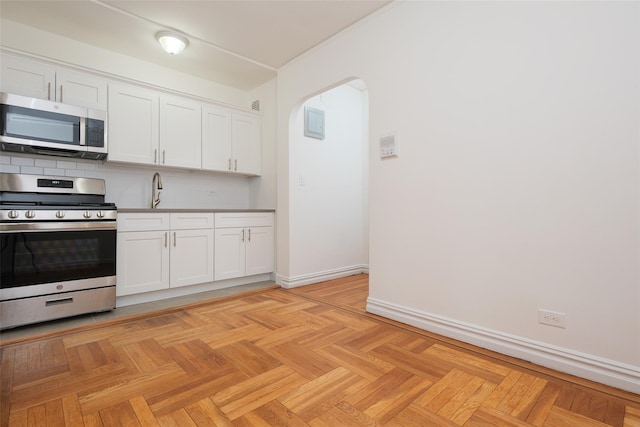 kitchen featuring arched walkways, baseboards, white cabinets, appliances with stainless steel finishes, and backsplash