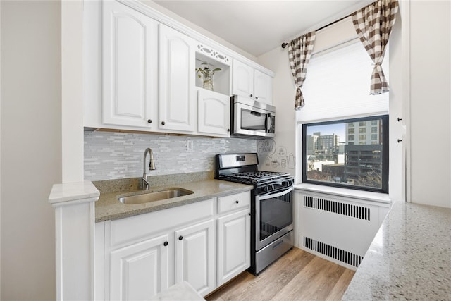 kitchen with white cabinets, decorative backsplash, radiator heating unit, stainless steel appliances, and a sink