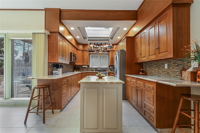 kitchen featuring a breakfast bar area, a skylight, appliances with stainless steel finishes, a kitchen island, and light stone countertops