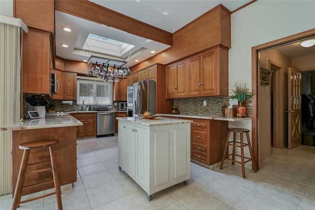 kitchen featuring a kitchen island, a skylight, a kitchen breakfast bar, a tray ceiling, and stainless steel appliances