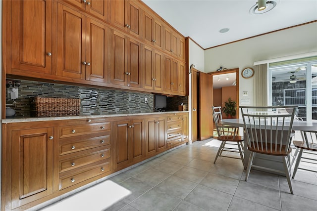 kitchen featuring light tile patterned flooring, ornamental molding, a kitchen breakfast bar, ceiling fan, and decorative backsplash