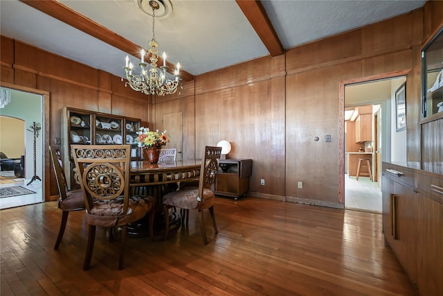 dining room featuring an inviting chandelier, beam ceiling, wood walls, and hardwood / wood-style flooring