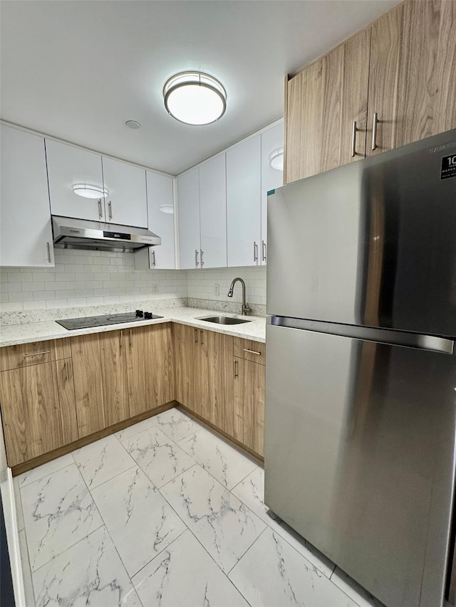 kitchen featuring sink, white cabinetry, black electric cooktop, stainless steel refrigerator, and backsplash