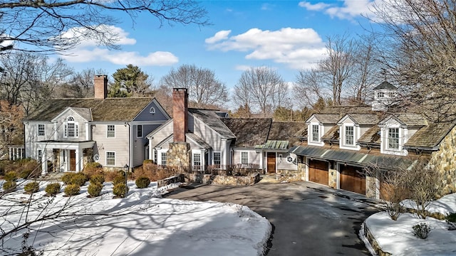 view of front facade featuring a garage, stone siding, aphalt driveway, and a chimney