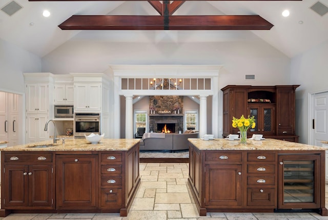 kitchen with stone tile floors, beverage cooler, stainless steel appliances, a sink, and a center island with sink