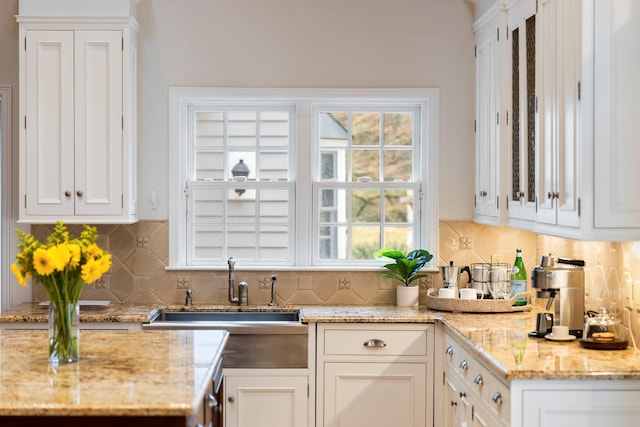 kitchen with white cabinets, a sink, decorative backsplash, and light stone countertops