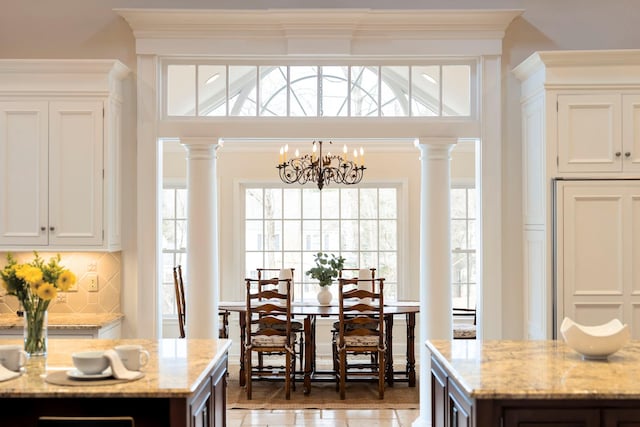 kitchen with crown molding, a chandelier, light stone countertops, and ornate columns