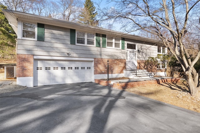 raised ranch featuring brick siding, aphalt driveway, and a garage