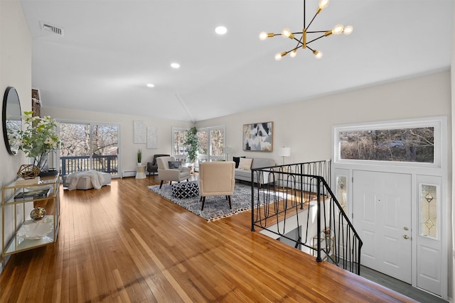 living area with visible vents, lofted ceiling, hardwood / wood-style flooring, a notable chandelier, and a baseboard radiator