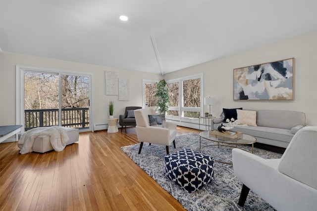 living room with a wealth of natural light, lofted ceiling, baseboard heating, and hardwood / wood-style flooring