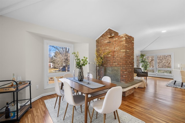 dining space featuring light wood-style floors, lofted ceiling, plenty of natural light, and a brick fireplace