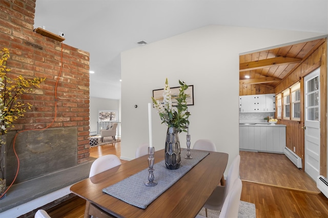 dining room with a baseboard heating unit, vaulted ceiling, wood finished floors, and visible vents